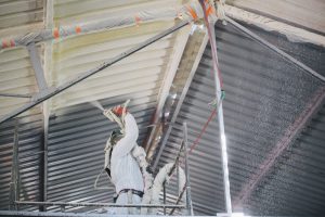 Pracownik Maremo wykonujący izolacje natryskową na suficie w hali.